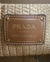 NEWSEDが販売するPRADAのラフィア製ミニバケットバッグ。レザーのロゴパッチにゴールドの刻印が施された詳細。