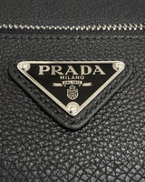 NEWSEDのPRADAブラックレザーバッグに施されたアイコニックなトライアングルロゴプレートのクローズアップ