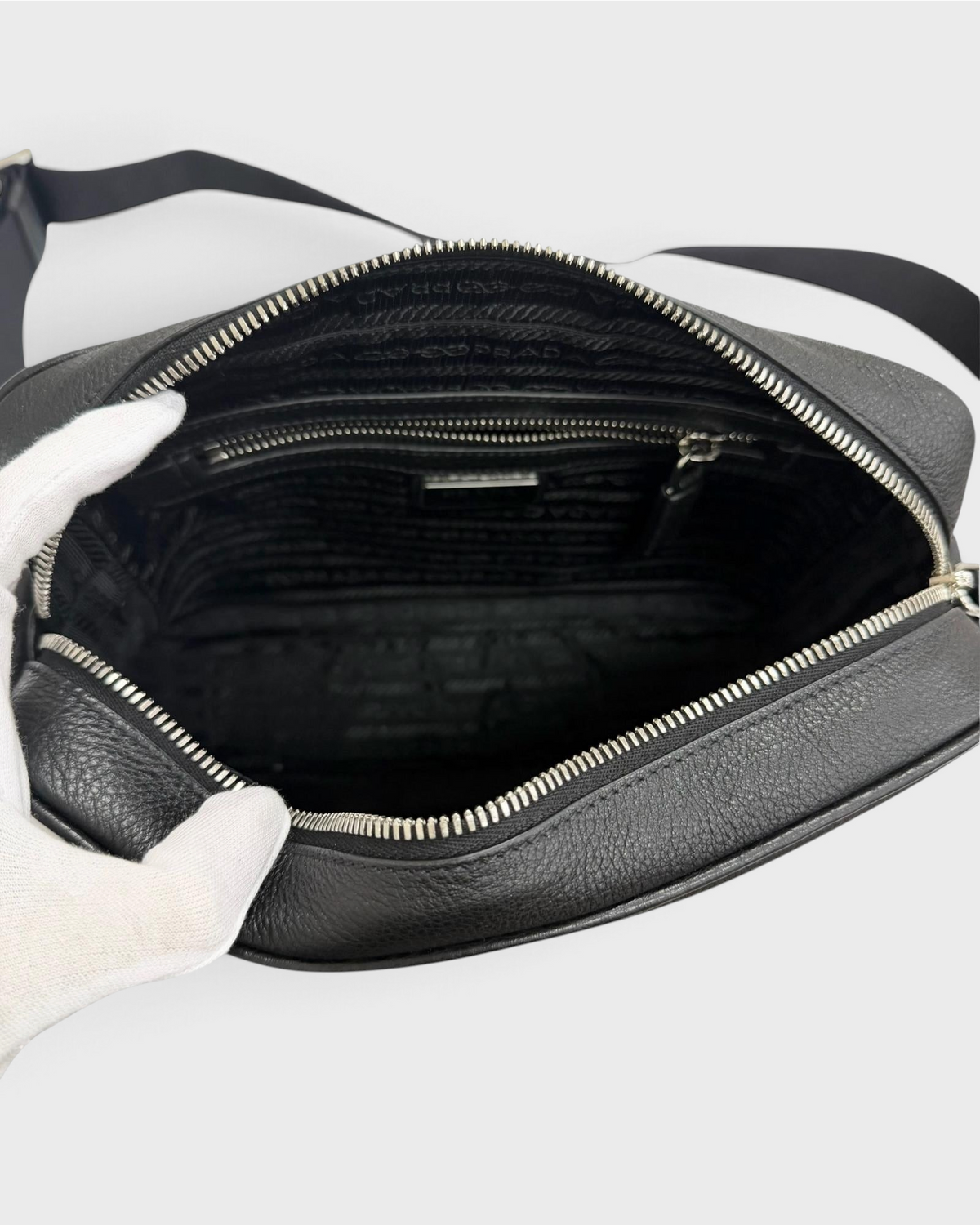 NEWSEDのPRADAブラックレザー製クロスボディバッグの内部、ファスナー付きポケットとロゴ入り裏地