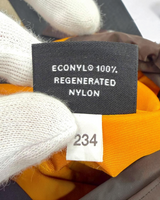 NEWSEDが取り扱うPRADAのRe-Nylonフォンポーチの内側タグ。ECONYL再生ナイロン100%の素材表記と製造番号が確認できるオレンジ色の生地。