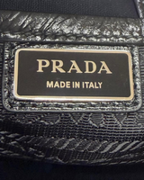 NEWSEDが販売するPRADAのブラックレザーショルダーバッグ。ブランドロゴプレートのクローズアップ。